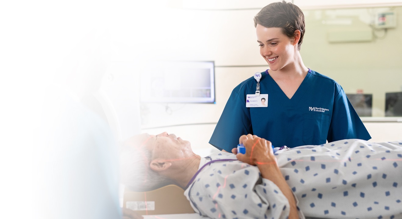 An elderly man laying down for a scan while talking to a female nurse wearing blue scrubs.